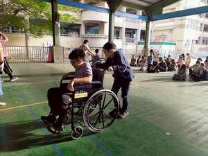 連結到六年級學生進行特教體驗活動，一位學生體驗肢障生坐在輪椅上指揮前進，一位學生體驗盲生推輪椅。(另開新視窗)